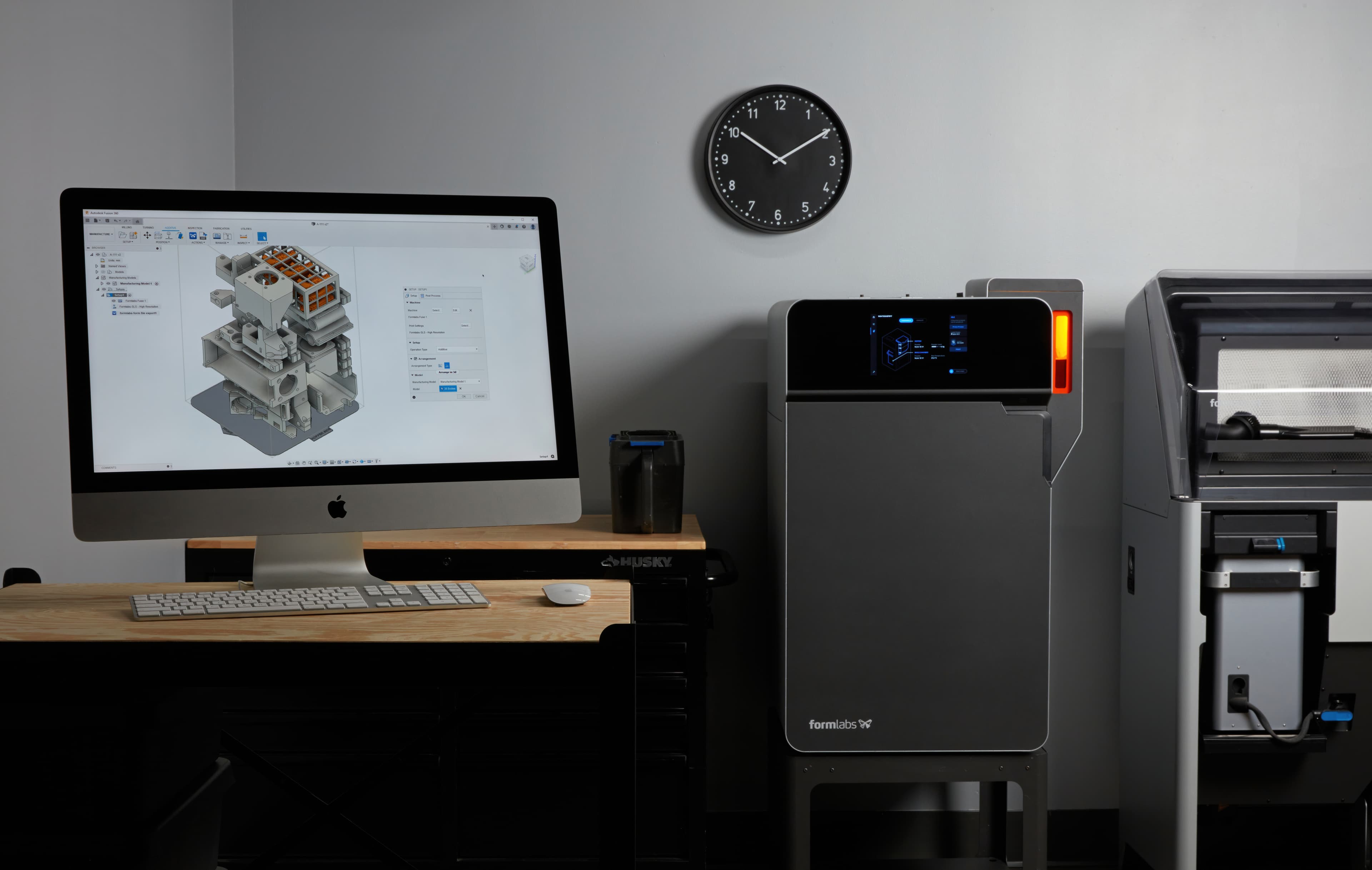 一台屏幕上显示 Autodesk Fusion 的电脑和一台 Fuse 系列 SLS 3D 打印机