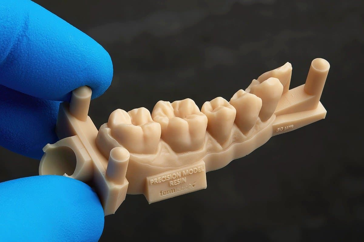 在黑色背景下,戴着蓝色手套的两根手指捏住在 Form 4 中使用 Precision Model Resin 制成的牙弓